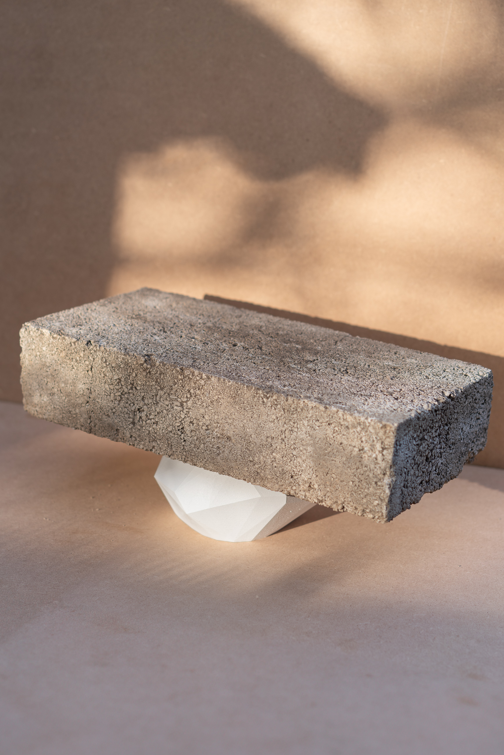 Compression - concrete block resting on white faceted form